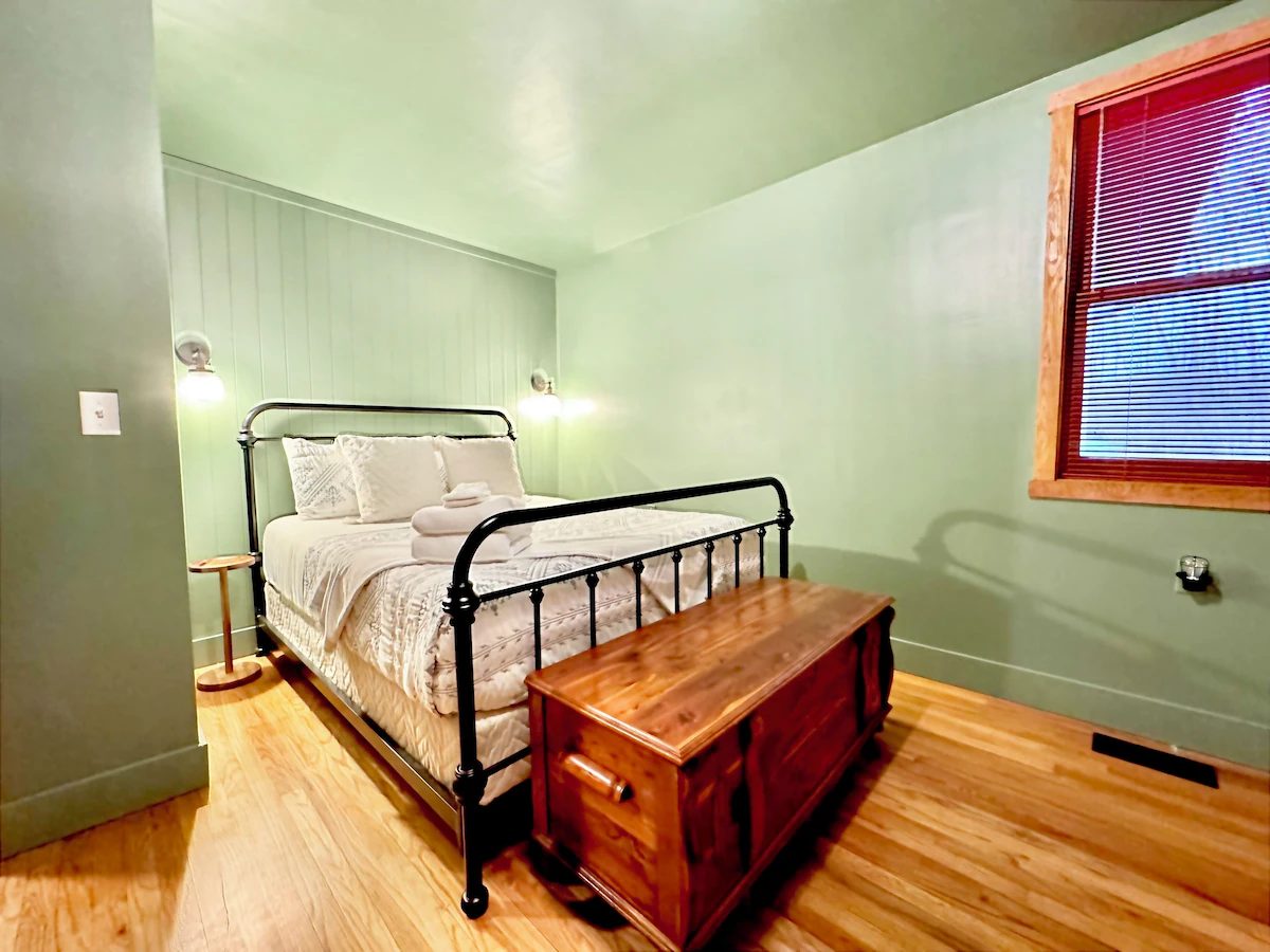Green-walled bedroom with a black metal bed frame and cedar chest