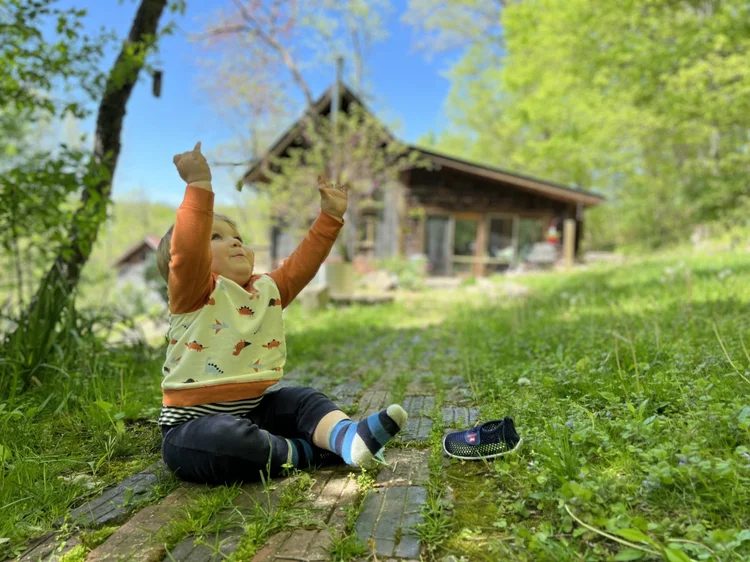 A small child sitting on the brick path in spring, the cabin behind