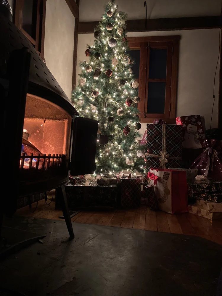 A lit Christmas tree and presents beside the wood stove