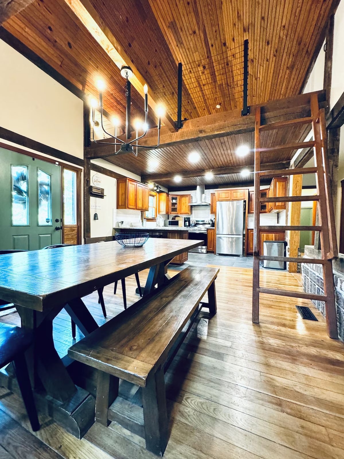 Dining table and benches under the wooden ceiling, with the ladder up to the loft
