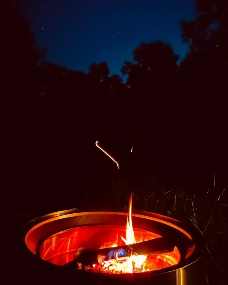A fire burning in the Solo Stove under a dark blue night sky and treeline