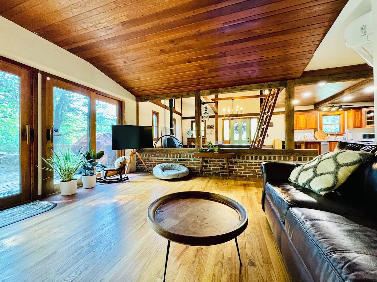 Living room with wooden ceiling, leather sofa and brick hearth, open to the dining area