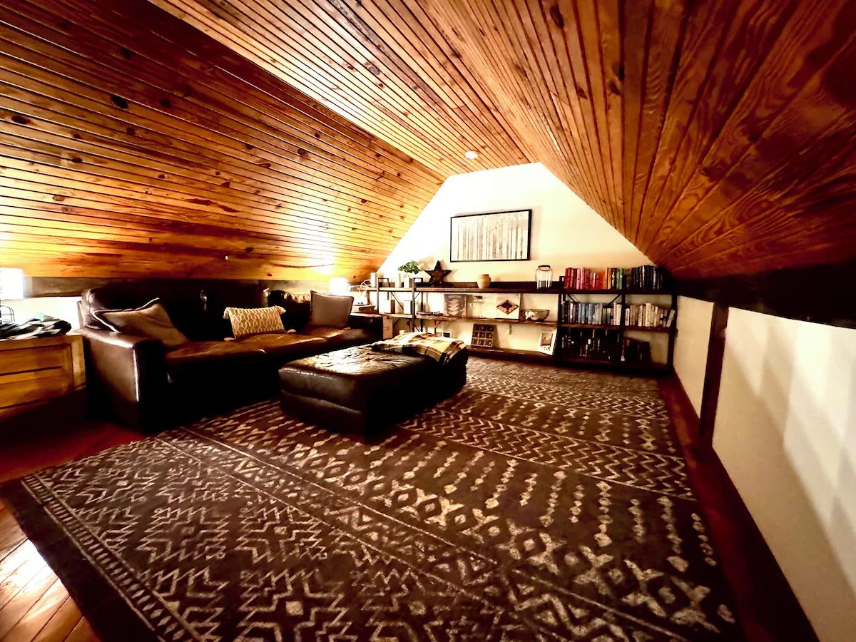 The loft under a pine ceiling with a leather sofa, bookshelves and a patterned rug